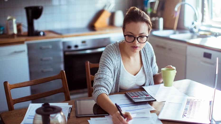 young woman paying bills at kitchen table